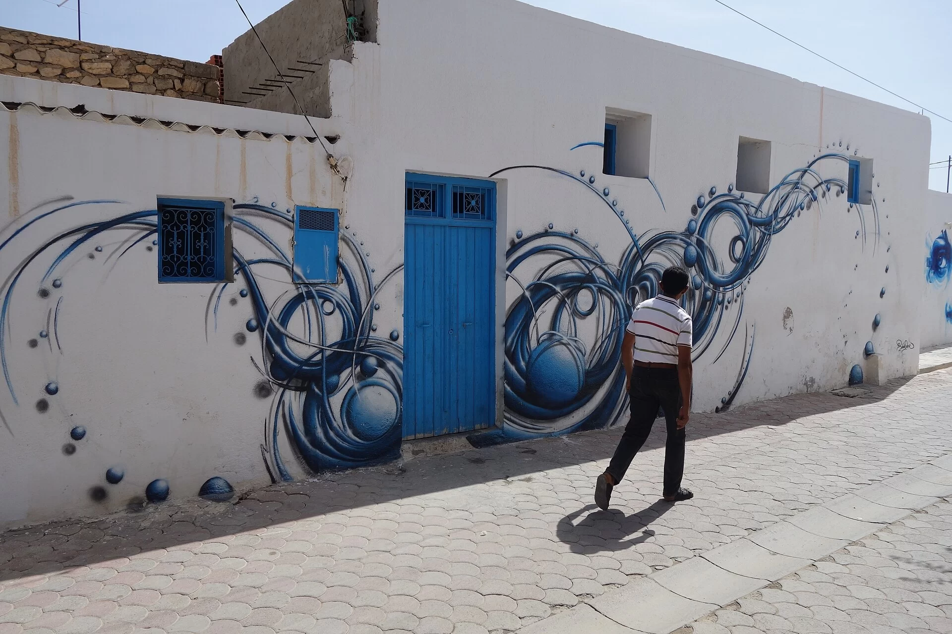 Une ruelle blanche ornée d'une fresque bleue à Djerbahood, sur l'île de Djerba